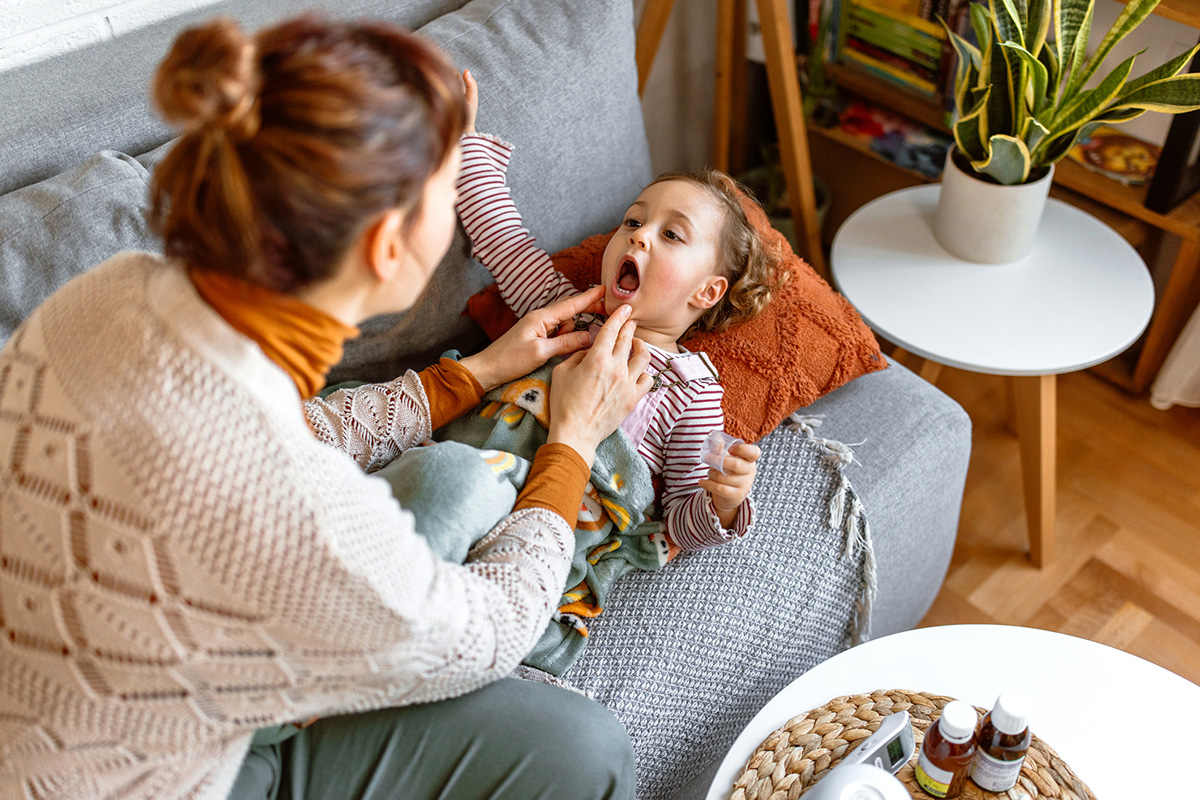 A worried mom looks in her daughter's mouth, checking for signs of strep throat.