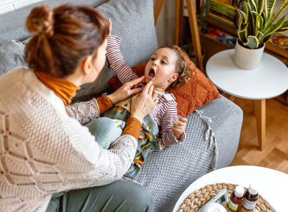 A worried mom looks in her daughter's mouth, checking for signs of strep throat.