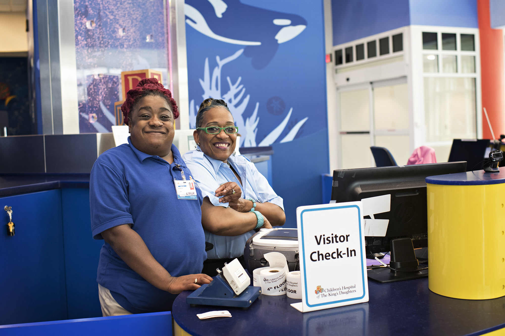 A volunteer and employee smile from the visitor check-in desk at CHKD