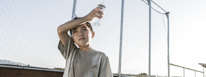 Young child excessively sweating in summer heat while trying to hydrate.