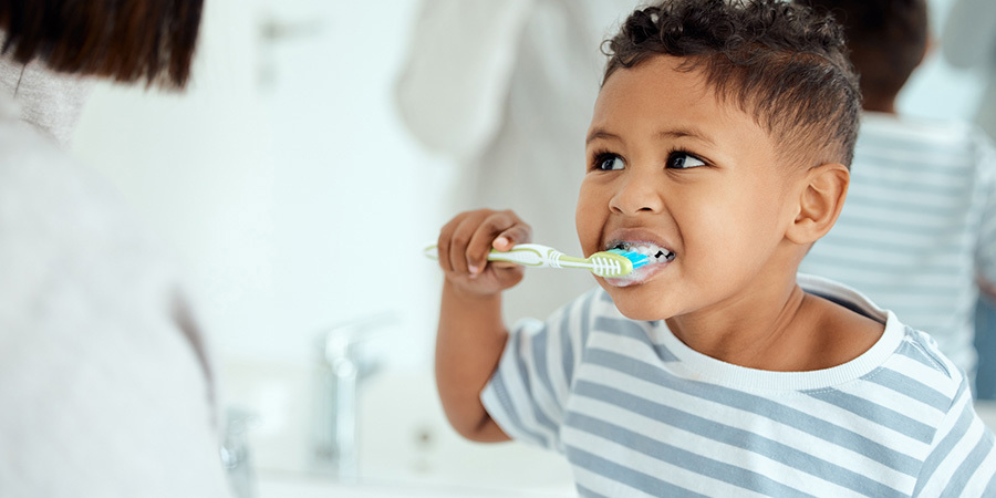 Shot of an adorable little boy brushing his teeth while his mother helps him at home