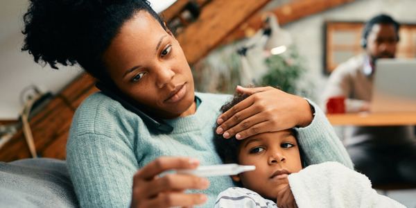 Worried mother talking on the phone while measuring son's temperature at home.