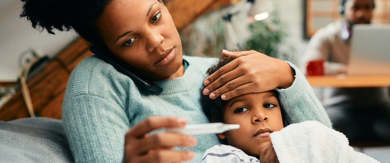 Worried mother talking on the phone while measuring son's temperature at home.