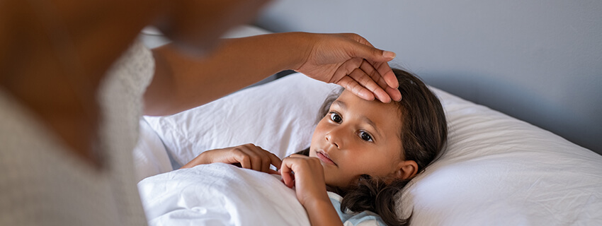 sick girl in bed with a caregiver touching her forehead