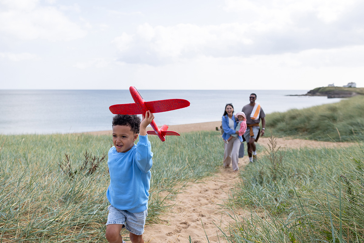 A wide shot of a joyful family walking up a sandy coastal path, surrounded by sand dunes at a beach