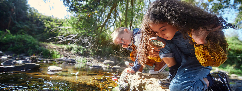 Young boy and girl looking at river with magnifier