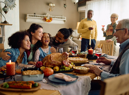 Happy multiracial parents and their kids laughing during family meal on Thanksgiving in dining room.