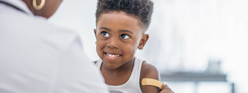 Young boy getting a bandaid on this arm by a doctor.