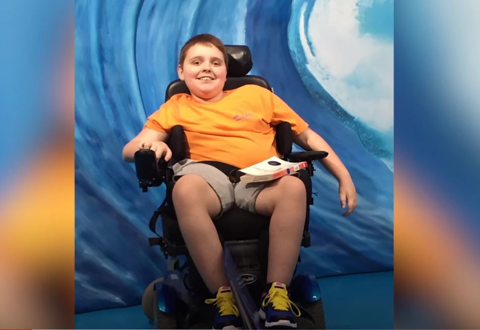 CHKD patient in a wheelchair wearing an orange shirt and shorts. 