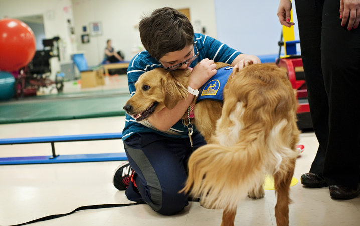 Patient Luke Orlando hugs facility dog SaraLee in the gym at CHKD.