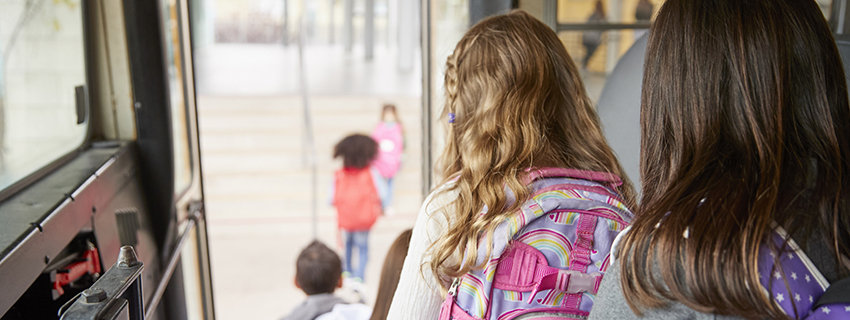 Children wearing backpacks getting off of the schoolbus.