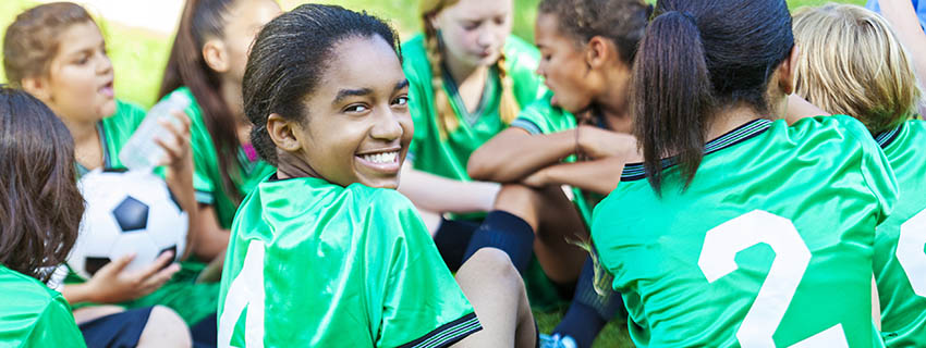 Girl in group of soccer players turns to smile at camera.