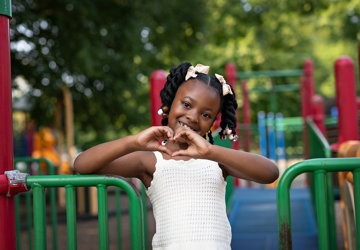 Patient Blessyn Watford making a heart with her hands on the playground.