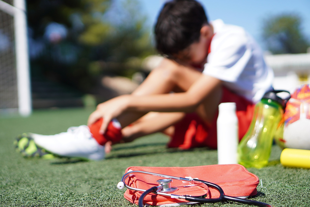 Blurred image of a child injured during soccer game holding his ankle in pain.