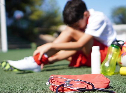 Blurred image of a child injured during soccer game holding his ankle in pain.