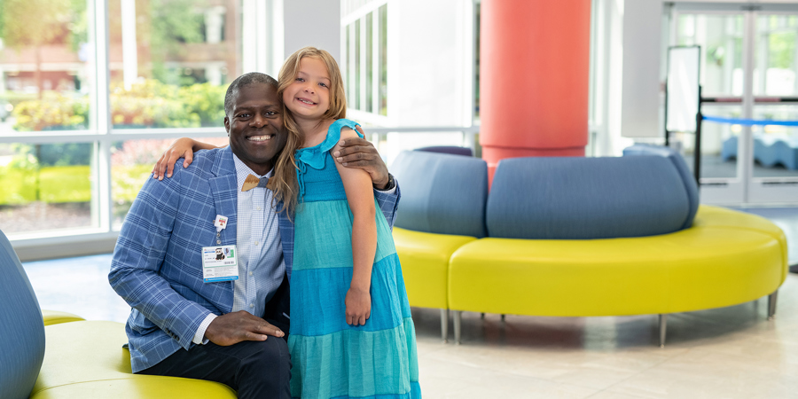 Parker Rose and her doctor, Dr. Carl St. Remy smile happily in the lobby at CHKD.