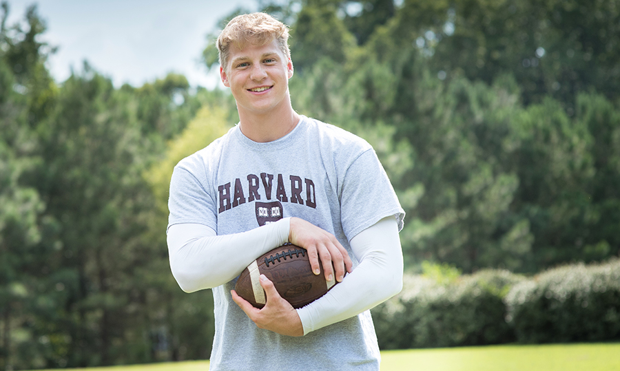 Portrait of Tyler Neville holding a football while wearing Harvard T-shirt.
