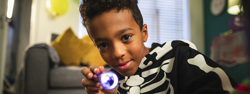 Child wearing skeleton pajamas shining a small light at the camera.