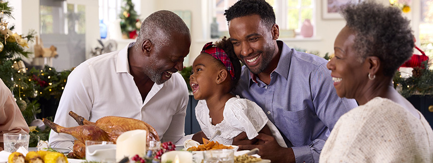 Grandparents, father, and daughter smile at Thanksgiving dinner.