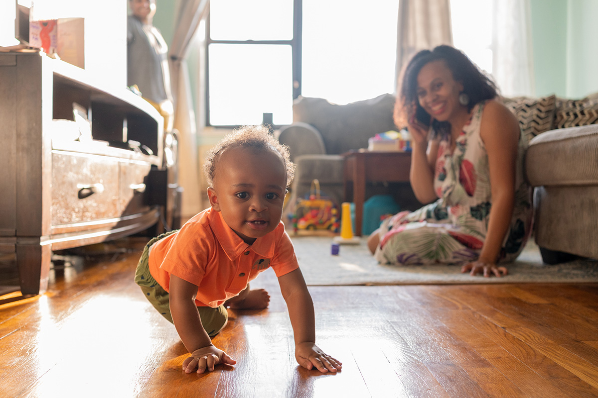 Baby crawling away as mom talks on the phone in the background.