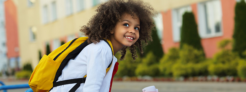 Girl wearing her backpack outdoors next to the school