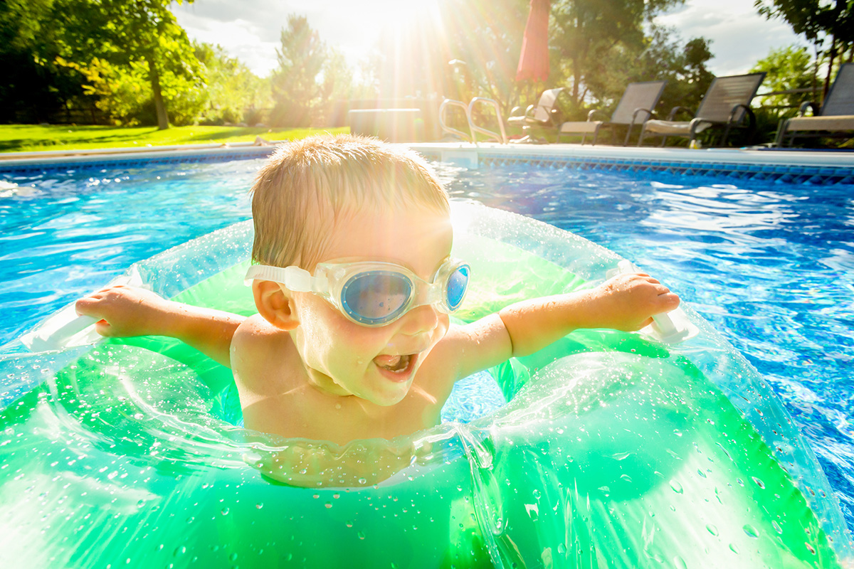 Close up of a little boy wearing goggles and using a tube float in the pool.