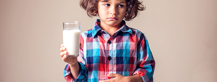 Young boy holding his stomach and making a pained face while holding a glass of milk.