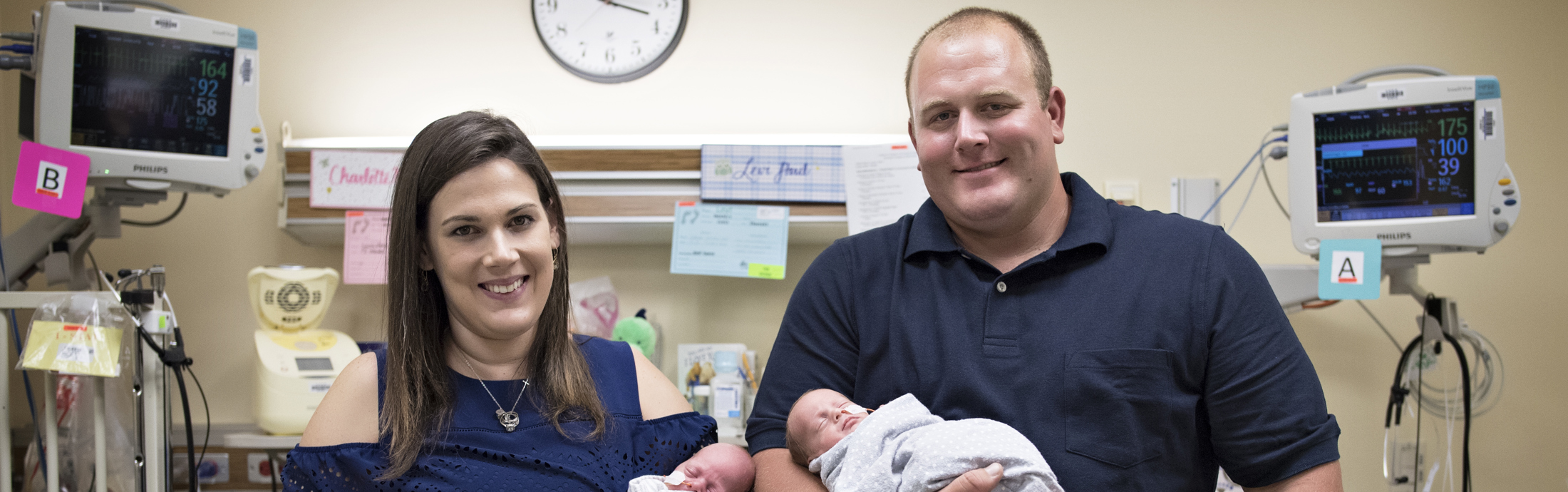 A mom and dad smiling together while holding their triplets in CHKD's NICU.