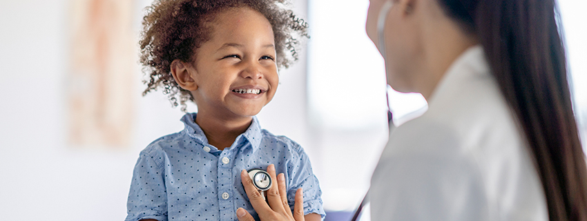 Doctor checking smiling child's heartbeat with stethoscope.