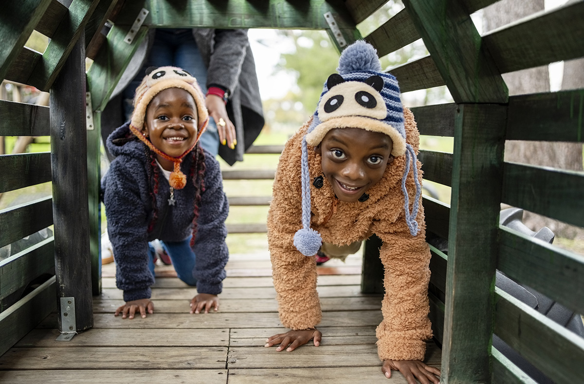 Two kids playing in a wooden tunnel on the playground
