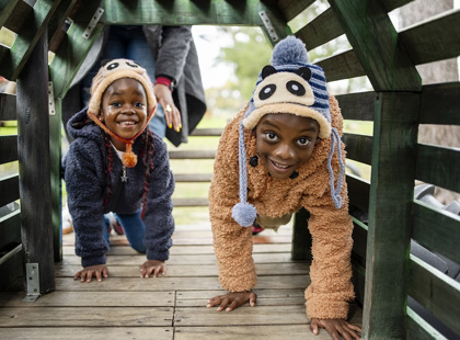 Two kids playing in a wooden tunnel on the playground