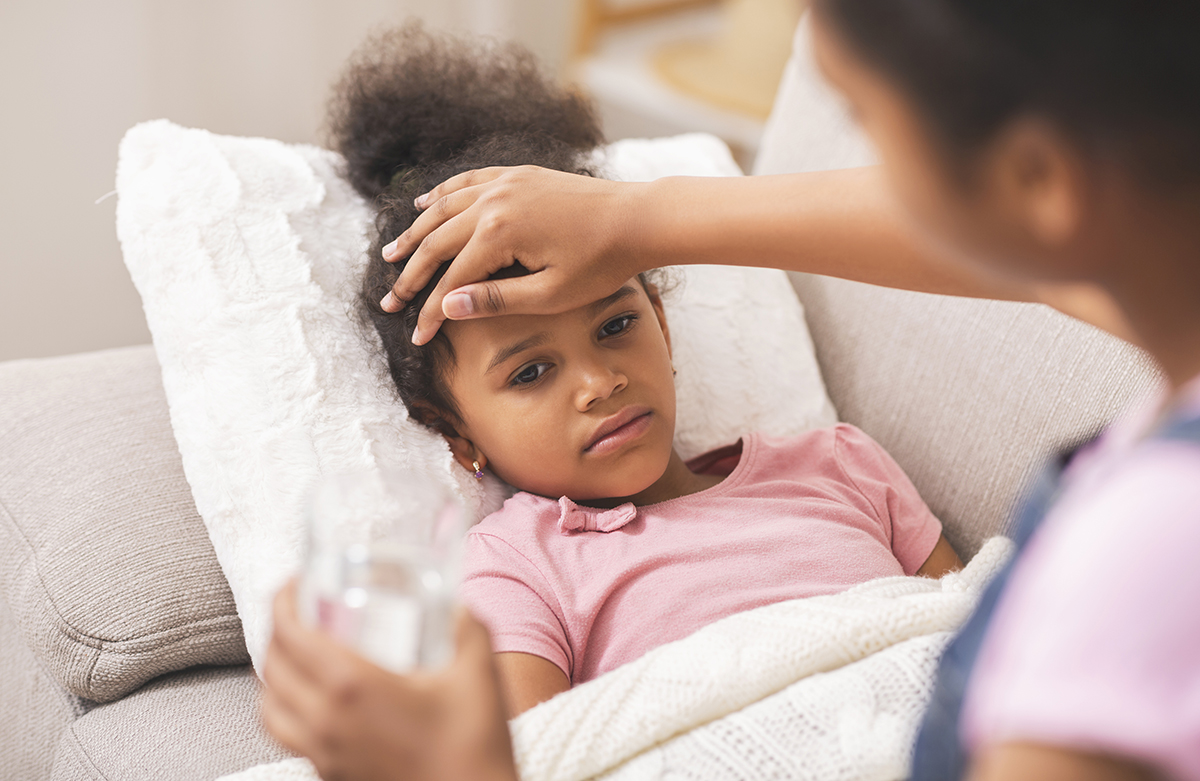 Caring mom giving water to her sick little daughter who is lying in bed.