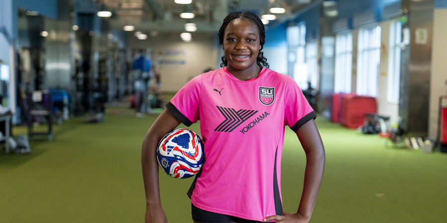 Madison Udoh in the CHKD Sports Medicine Gym with a soccer ball under her arm.