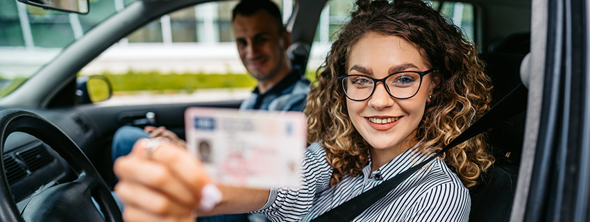Young female driving student holding up her new driver's license in the car.