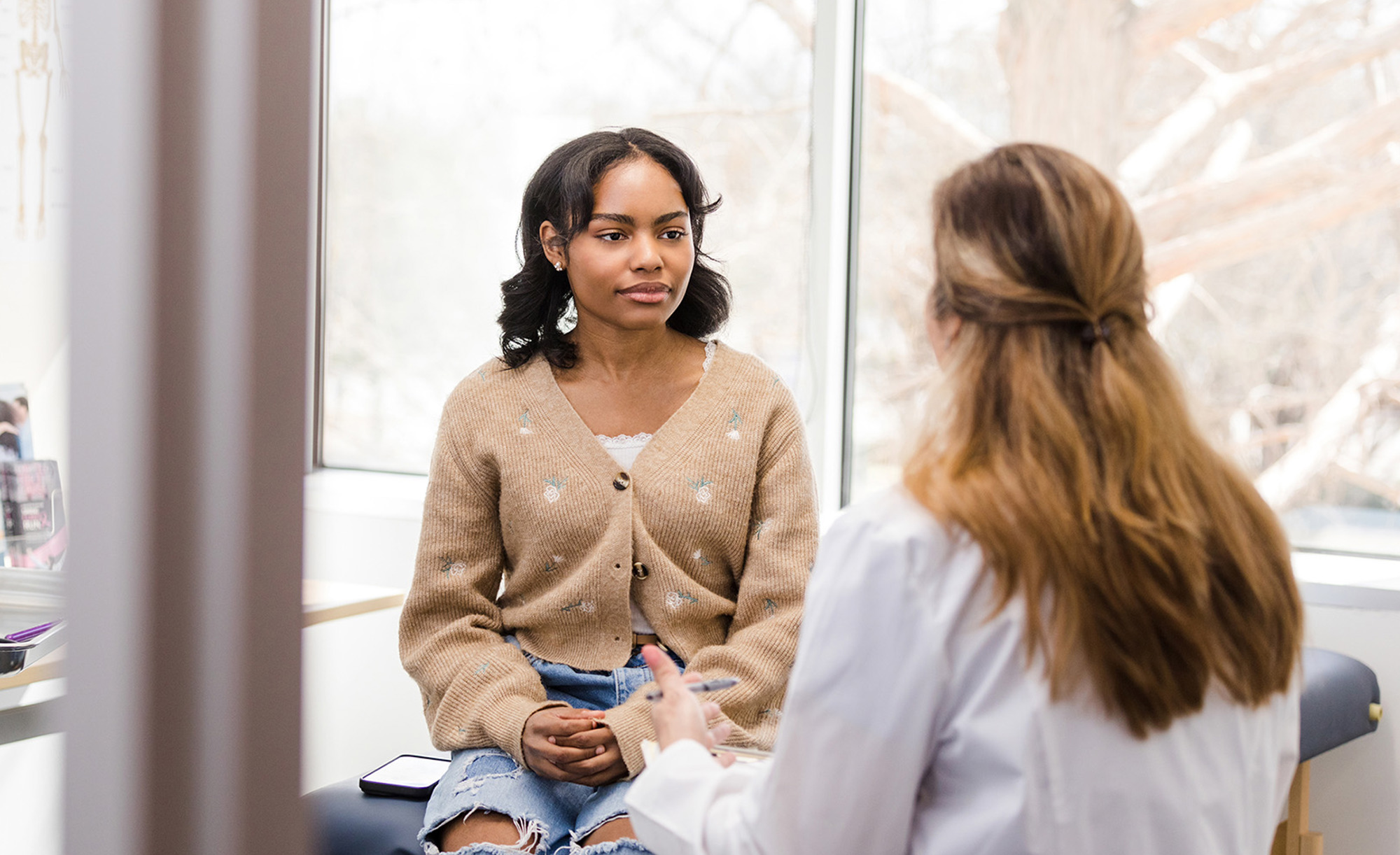 Female doctor gestures while talking to the young adult female patient about her symptoms