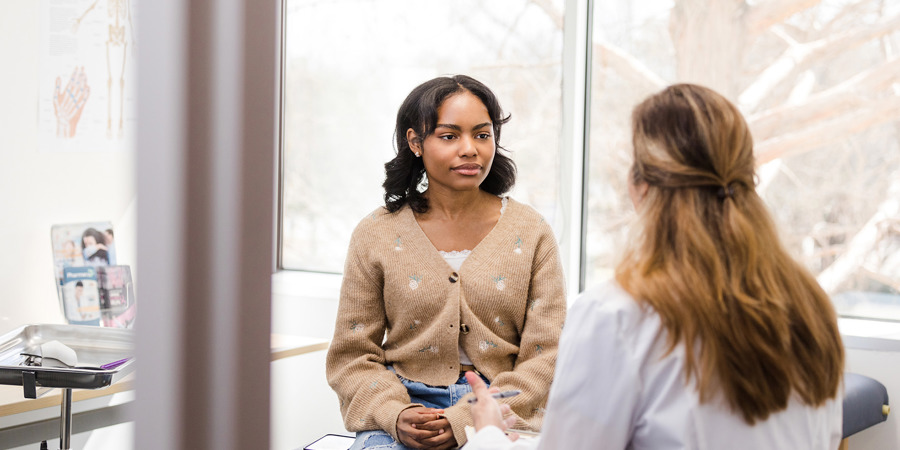 Female doctor gestures while talking to the young adult female patient about her symptoms