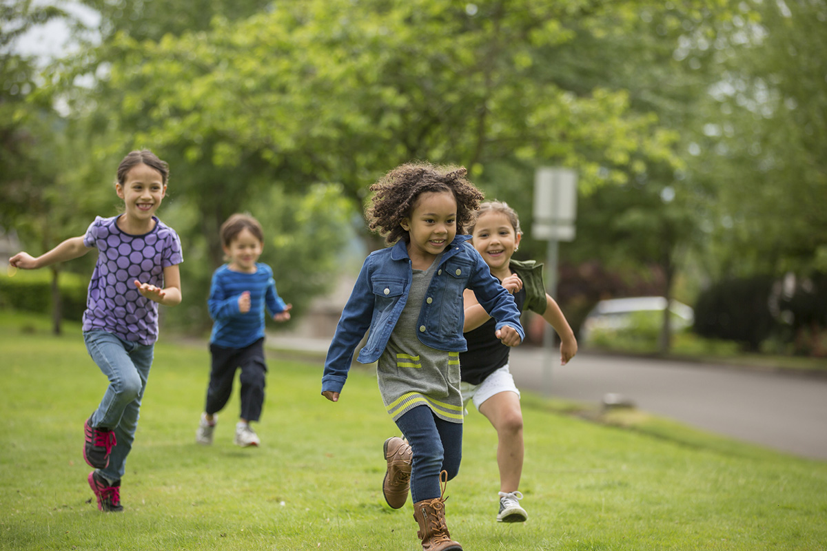Young diverse girls running and playing together in a neighborhood park.