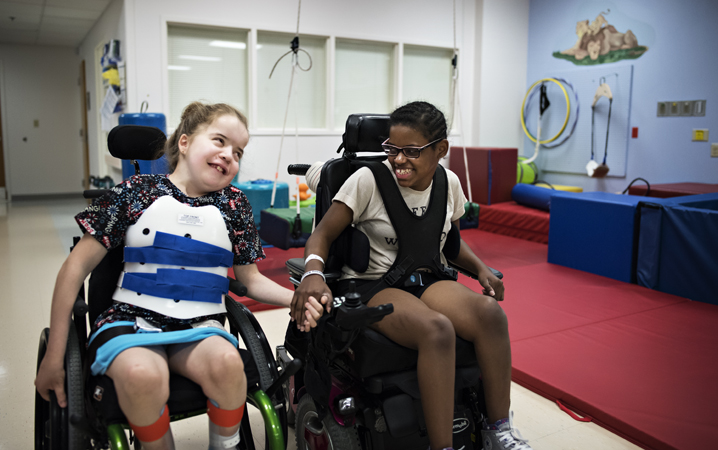Longtime friends and CHKD patients, Dana and Shelby hold hands and smile together while in their wheelchairs at CHKD.