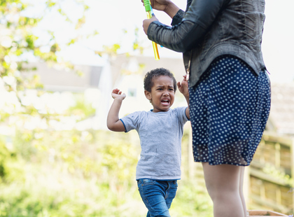A toddler boy screaming ad crying in disappointment about something his mother will not do. Mother is there too, but focus is on the boy. They are outdoors in backyard, it is summer