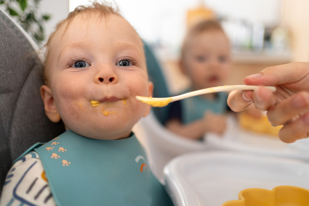 Close up of baby boy in his high chair enjoying his baby food.