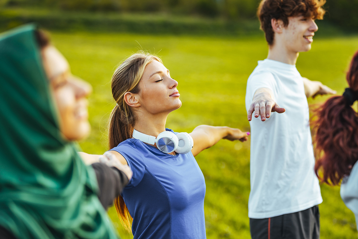 Group of teens doing breath exercising with stretched arms before game time or practice.