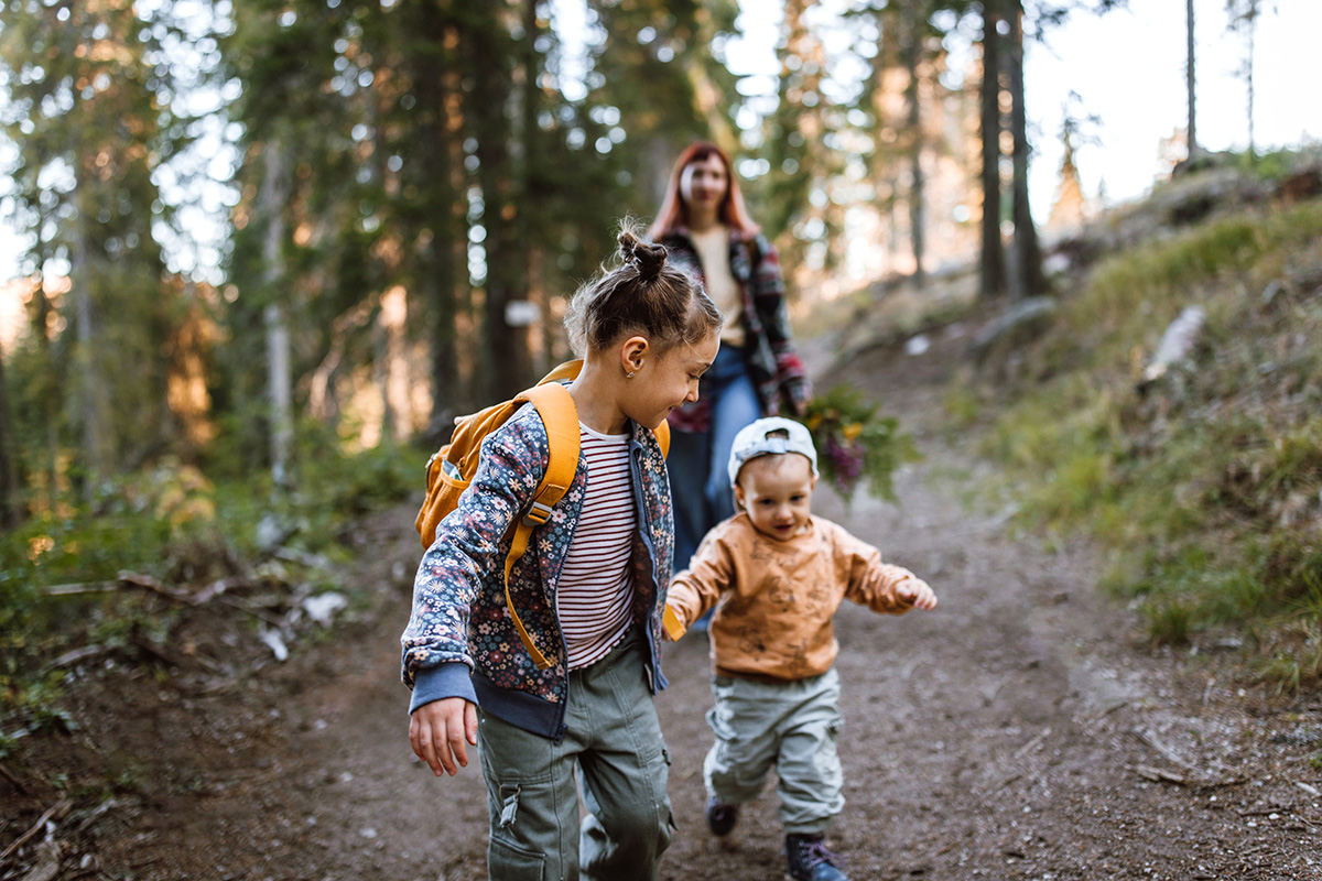 Photo of mid adult mother spending time with her children by taking them for a walk in wodland nature. Children holding hands and running around in forest.