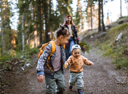 Photo of mid adult mother spending time with her children by taking them for a walk in wodland nature. Children holding hands and running around in forest.