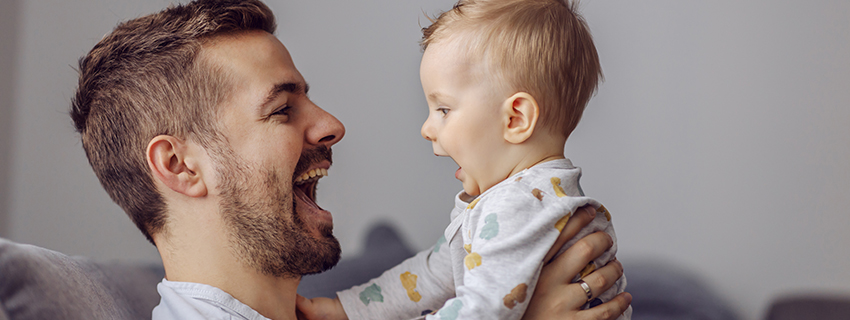 Smiling dad holds up baby to face each other. 